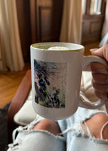 Load image into Gallery viewer, Person holding a white mug with a colorful design, sitting on a couch.

